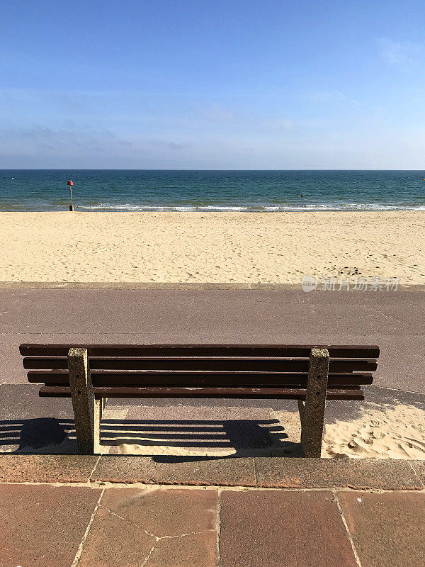 图片的海滨长椅俯瞰平静的大海，阳光明媚的蓝天和伯恩茅斯海滩/普尔沙洲，多塞特，英国，英国，石头混凝土和木制长椅的游客在英国海边度假坐下来享受vie